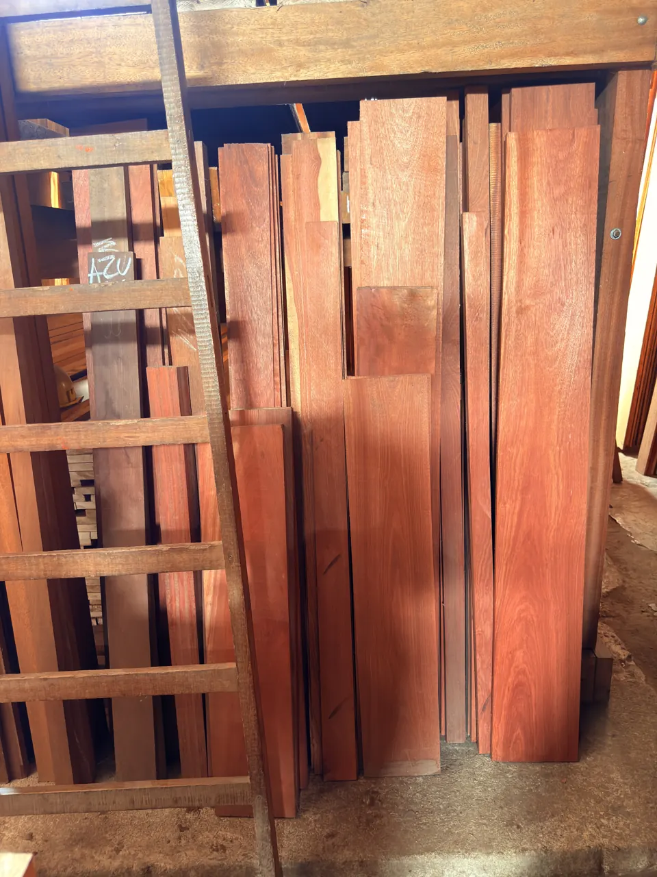 Escalera de madera apoyada en los estantes, delante de tablones rojizos de pie.