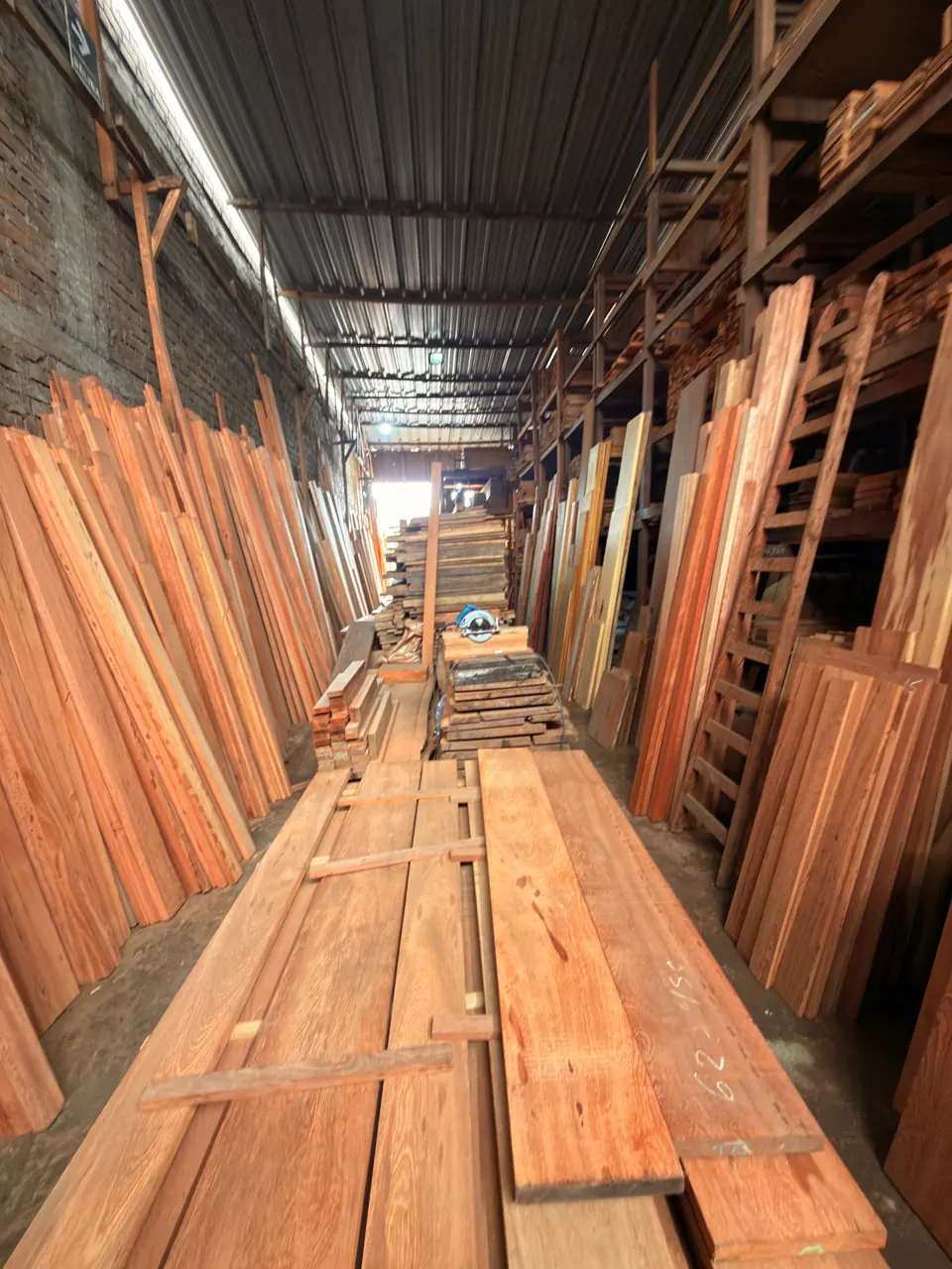 Pasillo largo del almacén, con tablas extendidas en el piso y tablones de pie a los lados.