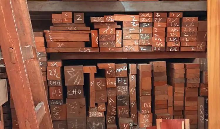 Estante del almacén con piezas de madera apiladas; en la cabeza de cada pieza, la medida o el nombre escritos a tiza.